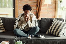 person sick blowing their nose sitting on the couch