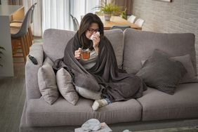 person with a cold blowing their nose sitting on a couch