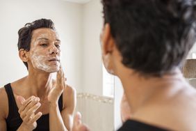 Young man washing his face in the mirror