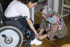 mother tying the shoe of her daughter with hemiplegia who is in a wheelchair