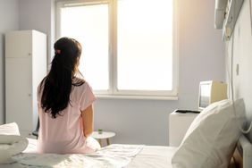 Female patient in hospital gown sitting on hospital bed facing window