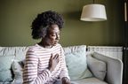 Black woman with hand on chest, wearing a white and pink striped shirt, sitting on couch