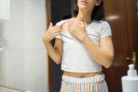 Female touching rash on chest wearing pajamas