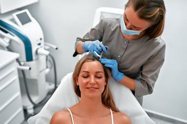 Mesotherapy, vitamin injections in head skin of hair area. Professional hair loss treatment. Close up view of woman head and doctor's hands with syringe.