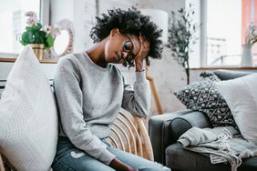 female holding her head with eveys closed sitting on a chair couch