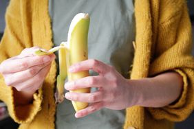 Person wearing a grey t-shirt and yellow sweater is peeling a banana