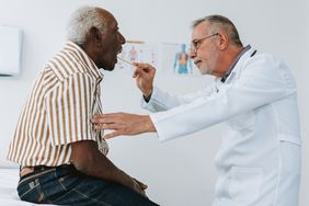White doctor looking in Black patient's mouth with tongue depressor