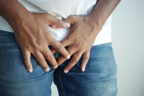 Close up of man pressing hands against groin area in discomfort or pain.