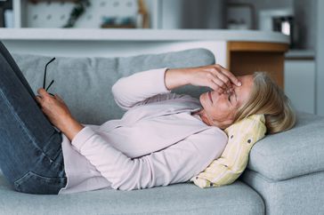 female with hand on forehead laying on couch