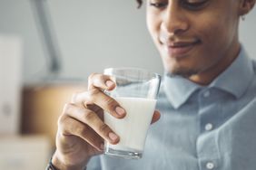 Young Black man wearing a button down shirt holding a glass of milk