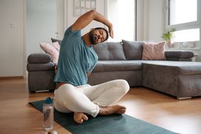 Man wearing blue tshirt and white sweatpants stretching on an exercise mat at home in his living room