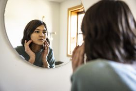 teenage girl examining skin in mirror