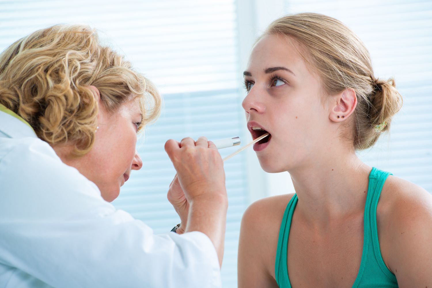 Doctor checking teenage girl's throat with a tongue depressor