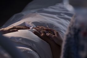 shot of person's hand on older person's hands in hospital bed no faces