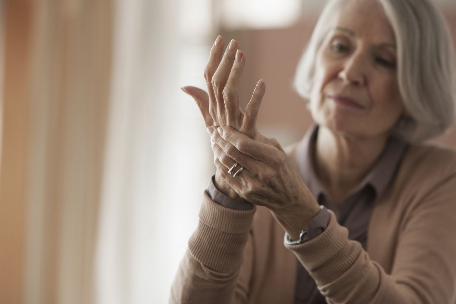 Older women wearing a tan sweater rubbing her hands in pain. 