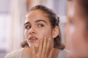 Girl looking into a mirror and touching her face to examine her skin.