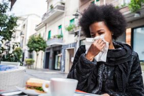 Woman sneezing due to cold during a break in a cafe using an handkerchief