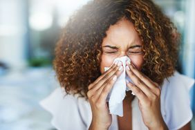 female blowing her nose into a tissue with eyes closed