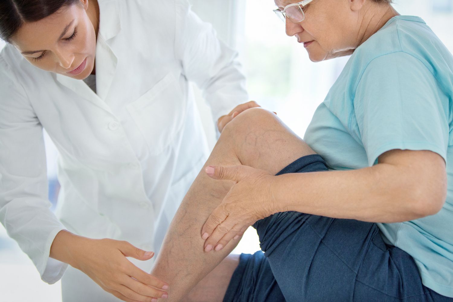 Closeup side view of doctor massaging legs and calves of a senior female patient with visible varicose veins.