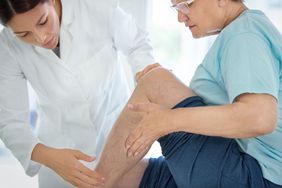 Closeup side view of doctor massaging legs and calves of a senior female patient with visible varicose veins.