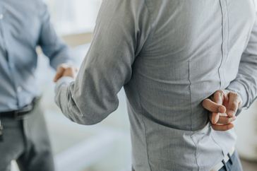 Two men shake their hands in a business deal. One of the men has his finger crossed behind his back, hinting at dishonesty.