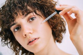 A young woman applying a glycolic acid serum to her face with a pipette