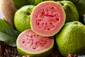 Closeup of a red guava cut in half, in the background several guavas and green leaf