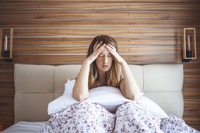 A young women in bed with a headache on top of head
