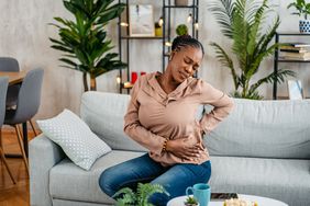 Young black woman sitting on the couch with back and stomach pain