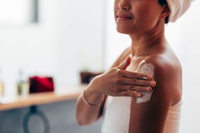 Woman wearing a towel applying skincare to her arm