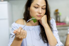 Woman holds up cilantro leaf with a fork and frowns