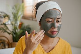young Asian woman applying clay mask to her face at home