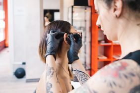 Tattooist piercing ear of customer in parlour 