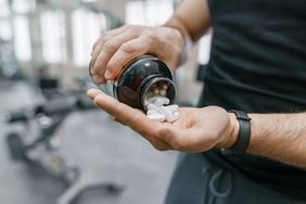 Closeup of a white man in a gym pouring a bottle of supplement pills for muscle growth into his palm
