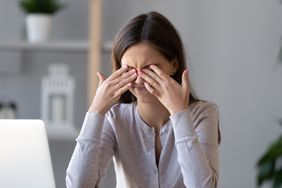 A woman holds her hands up to her eyes as she scrunches her face in pain