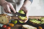 Person spreading avocado toast on whole wheat bread.