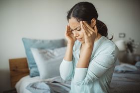 Person with a headache holds their temples in pain in their bedroom.