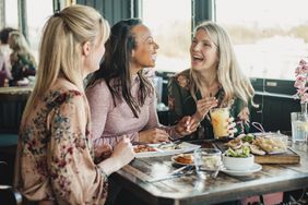 A group of female friends laugh as they sit at a restaurant table 