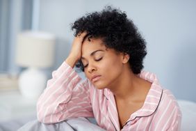Person in bed puts hand to head and looks tired.