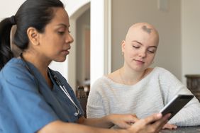 An adult female with Alopecia is being helped by her Hispanic female nurse