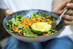 Close up on a person holding a bowl with an alkaline, plant based meak: Salad, chickpeas, beans, avocado
