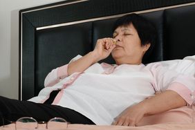 A woman lies in her bed and puts smelling salts up to her nose