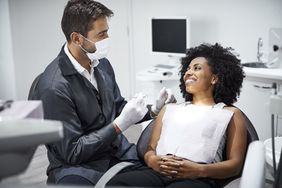 A white male dentist is examining a black female patient in a dentist clinic.