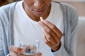 Close-up of person taking supplement pill with water.
