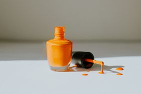 Bottle of orange nailpolish with drops of it on the table