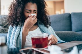 Person blowing their nose while sick with a cold at home.