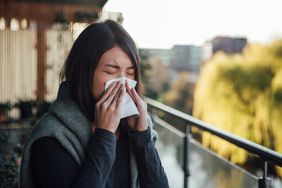 Head shot of young woman having allergy symptoms, covering her nose with tissue while sneezing.