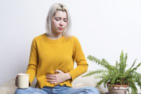 A young woman sits cross-legged with her hand on her stomach