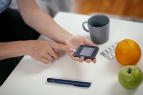 A person tests their blood sugar with an orange and apple next to them