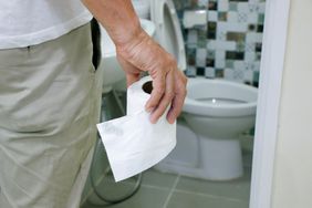 A man walks into a bathroom holding a roll of toilet paper